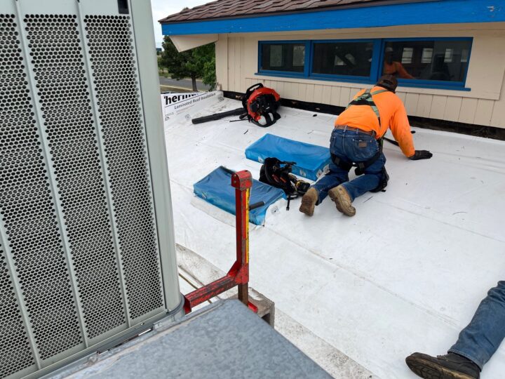 showing a commercial roofer for JRC Roof Services on his hands and knees laying roofing